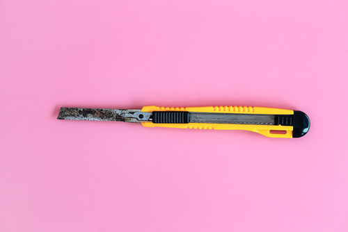 Rusty yellow paper knife isolated on pink background