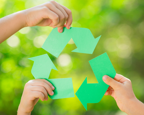Paper RECYCLE sign in children`s hands against green spring background. Earth day concept