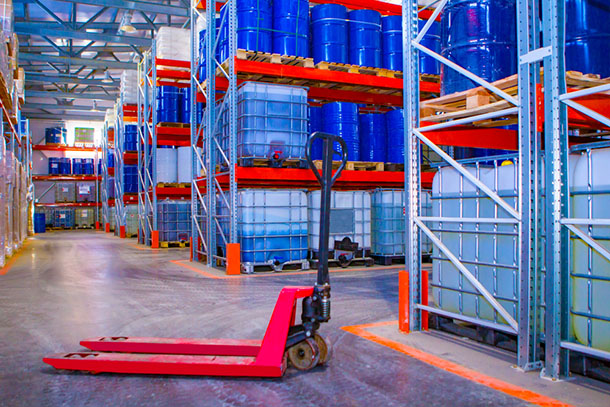 a pallet jack in a warehouse with oil barrels and plastic chemical containers