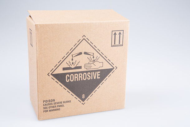 abrown cardboard box with a corrosive danger logo printed on it